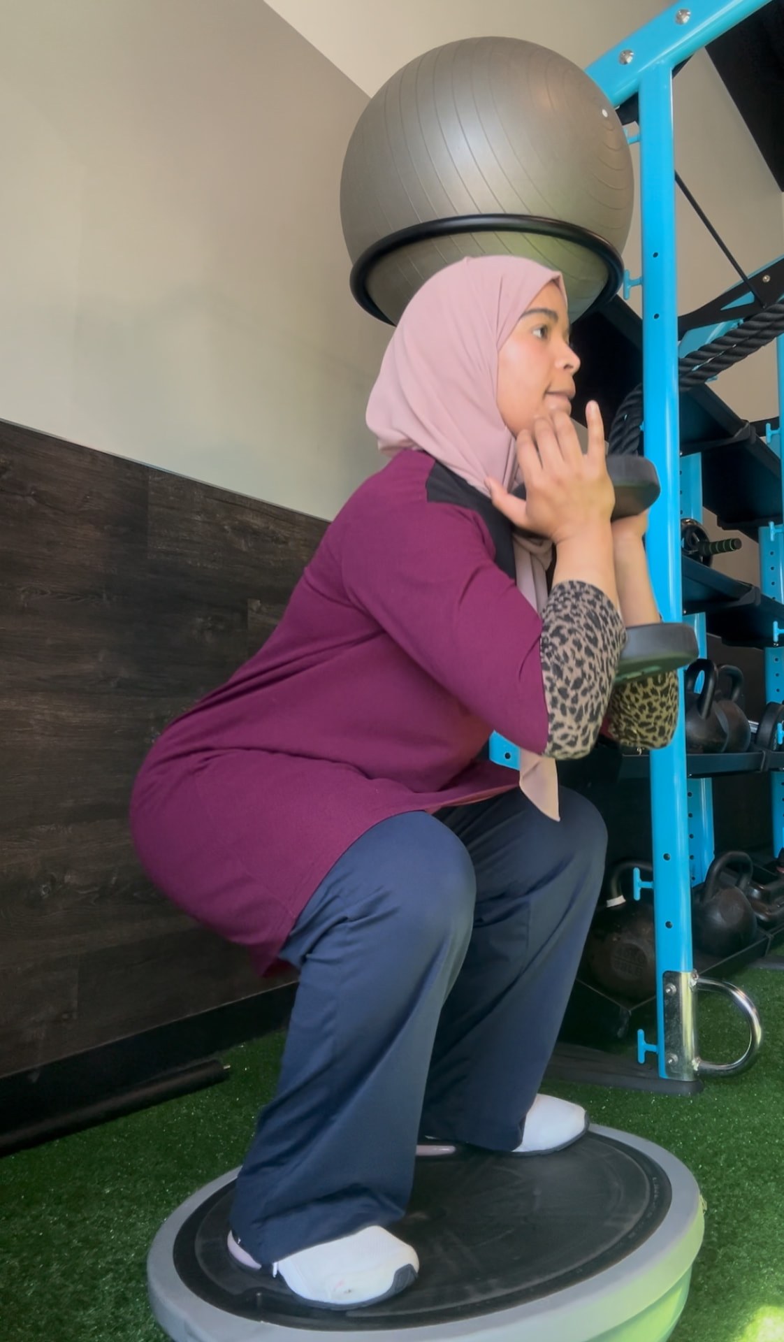 Coach Assia performing a goblet squat on a balance trainer with a dumbbell