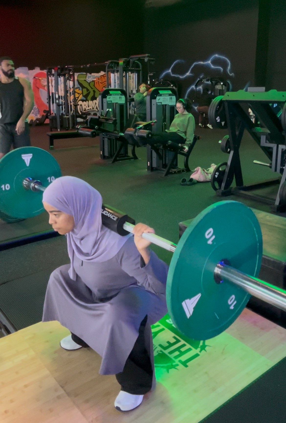 Coach Assia performing a barbell back squat with controlled form in the gym
